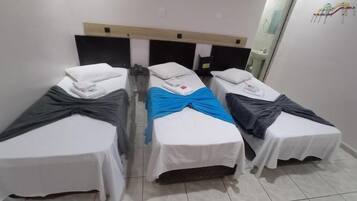 Quarto de hotel com três camas de solteiro, cada uma com colcha branca e manta escura.