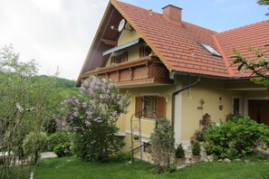 A two-story house with a sloped roof, a balcony, and a garden with flowering plants. - 1 in the romantic guesthouse Annas-Home (Ratsch)
