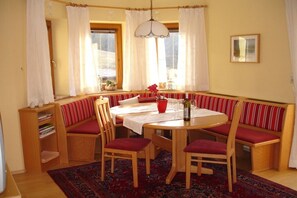 En matplats med ett runt bord, trästolar, en bänk med röda kuddar, en röd vas och en mönstrad matta.