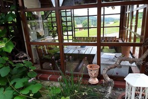 A conservatory with a view of a garden, a wooden table, and a decorative pot. - 1 in the romantic guesthouse Annas-Home (Ratsch)