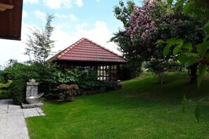 A gazebo with a red roof, surrounded by lush greenery and a flowering tree. - 1 in the romantic guesthouse Annas-Home (Ratsch)