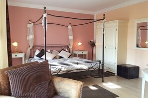 Un dormitorio con cama con dosel, un aparador, una mesita de noche con lámpara y un taburete pequeño.