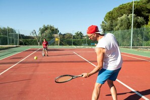 A tennis court with a net, a player in a white shirt and blue shorts, and another player in a red shirt. - Hotel Villaggio Mira (Peschici)