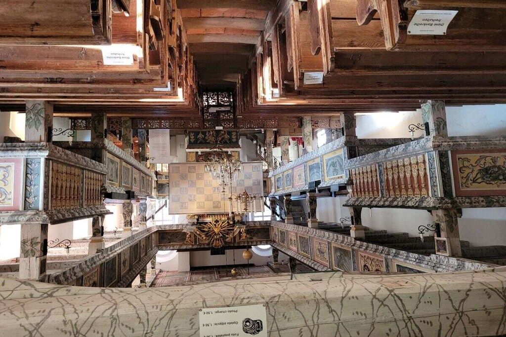 An interior with a central staircase, wooden beams, and patterned walls.