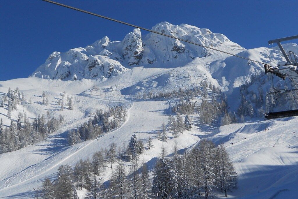 Eine verschneite Berglandschaft mit einer Seilbahn und Bäumen.