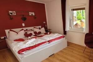 Un dormitorio con cama blanca, detalles en rojo, una ventana con vistas y una silla roja.