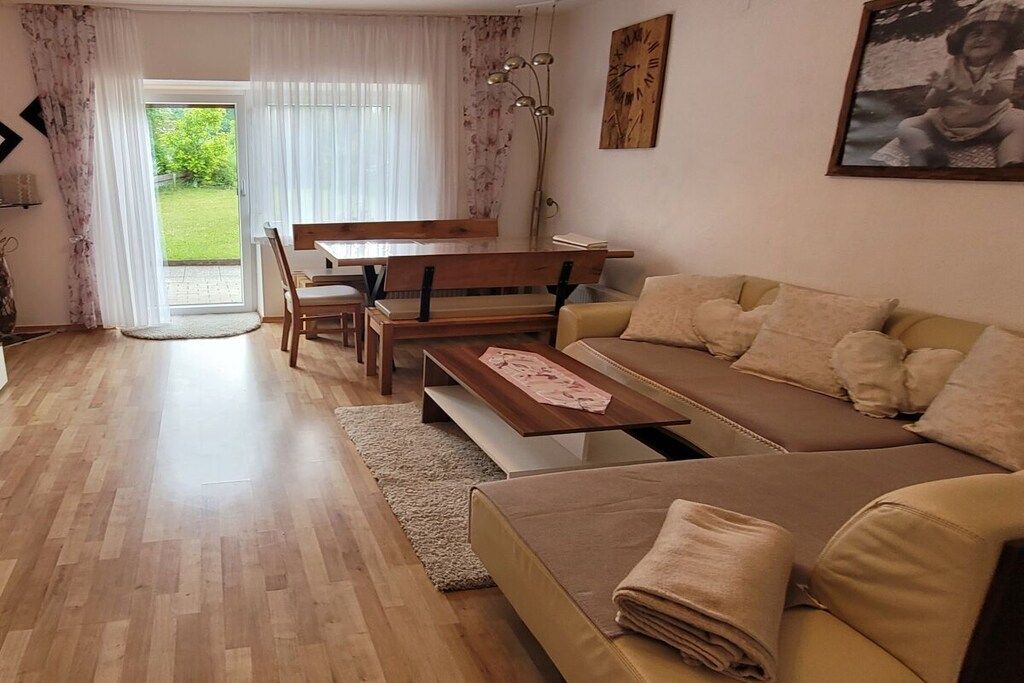 A living room with a sofa, a coffee table, a dining table with chairs, and a large window with curtains.