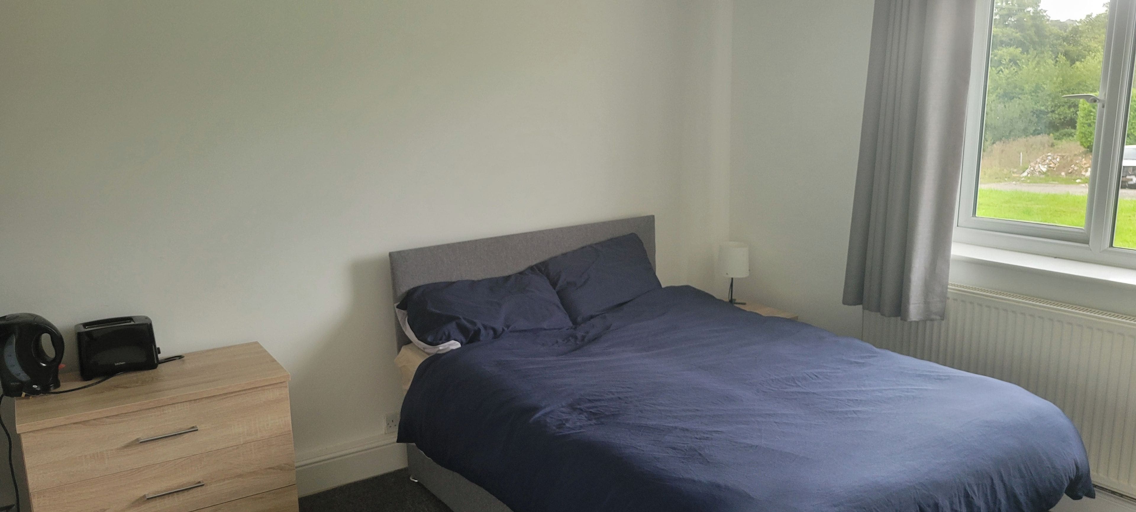 A bedroom with a bed, a bedside table, a lamp, and a window with curtains.