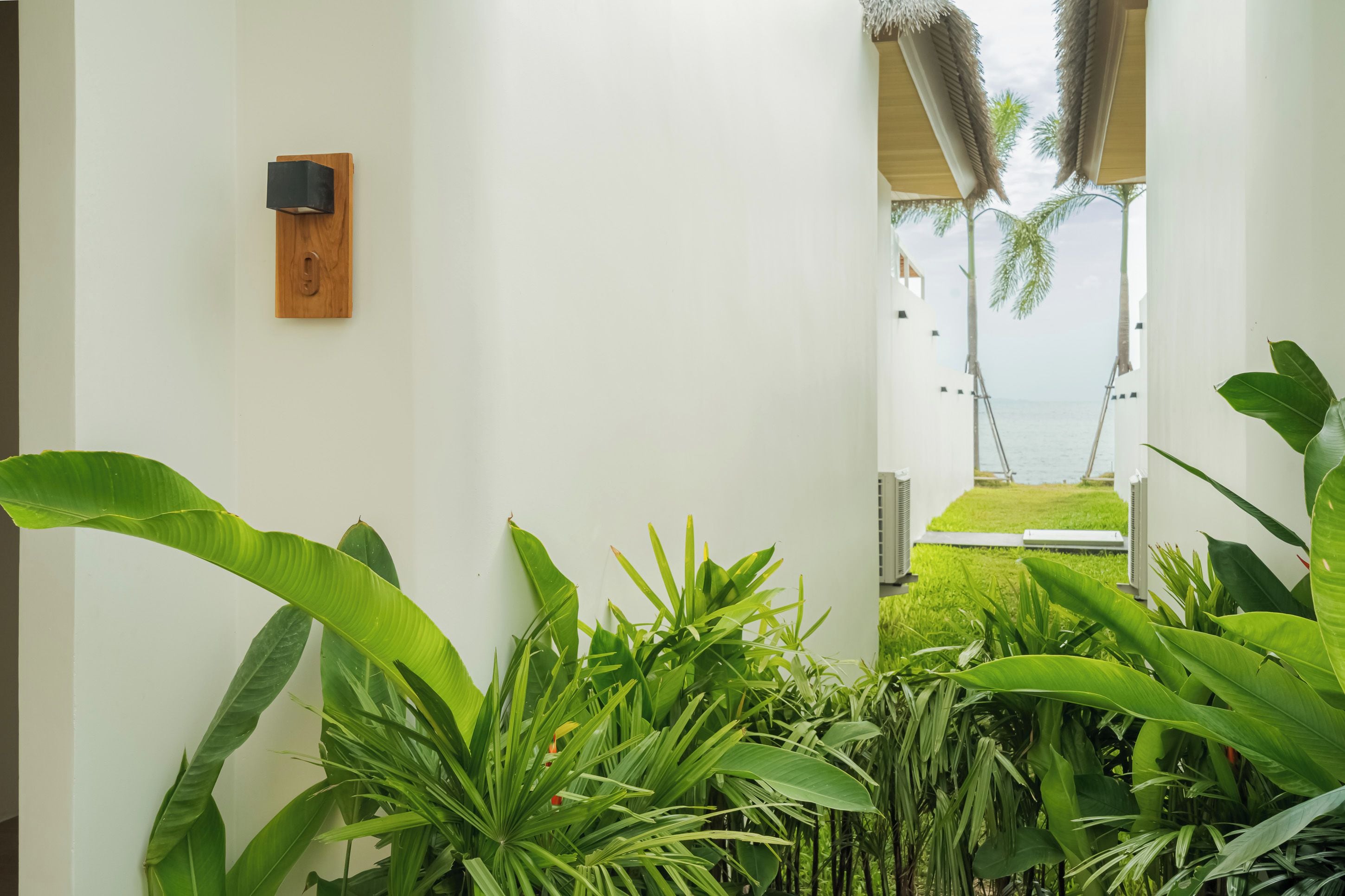 Pasillo con vistas a la playa, plantas de interior y una lámpara de madera fijada a la pared.