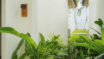 Pasillo con vistas a la playa, plantas de interior y una lámpara de madera fijada a la pared.