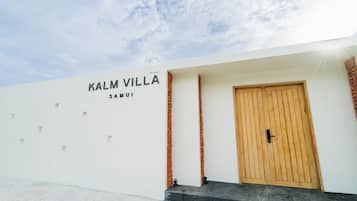 Un edificio con un letrero que dice 'KALM VILLA SAMUI' y una puerta de madera.
