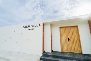A building with a sign reading 'KALM VILLA SAMUI' and a wooden door.