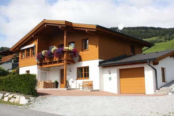 A two-story wooden house with a balcony, a garage, and a gravel driveway.