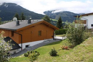A wooden cabin with a sloped roof, surrounded by a well-maintained lawn and a mountain backdrop.