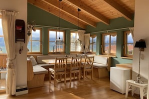 A cozy room with a wooden ceiling, large windows, a dining table with chairs, and a white cabinet.
