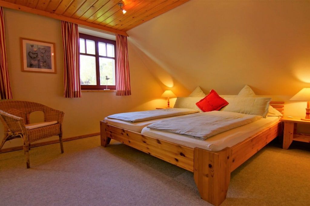 Un dormitorio con una cama de madera, dos mesitas de noche, una silla y una ventana con cortinas.
