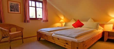 Ein Schlafzimmer mit einem hölzernen Bett, zwei Nachttischen, einem Sessel und einem Fenster mit Vorhängen.