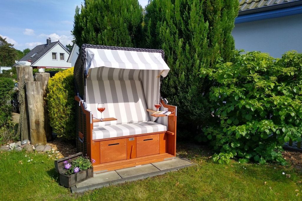 A wooden outdoor seating area with a striped canopy, a cushioned bench, and a wine glass.