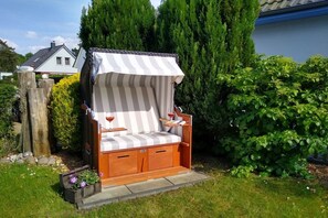 A wooden outdoor seating area with a striped canopy, a cushioned bench, and a wine glass. - Holiday home with 1 bedroom (Ostseebad Prerow)