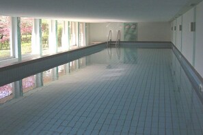 Ein Innenpool mit großen Glaswänden, gefliestem Boden und einer Leiter an einem Ende.