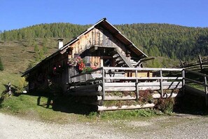Ein rustikales Holzhäuschen mit Balkon, umgeben von einem Holzzaun und einer Berglandschaft.