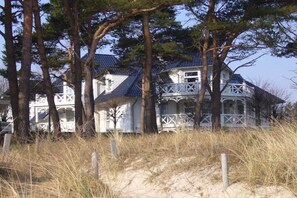 Ein Küstenhaus mit Balkon, umgeben von B äumen und Sand.