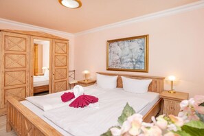 A hotel room with a bed, wooden wardrobe, a painting, and two bedside lamps. - "Beach Promenade" - Haus Strelasund (Ostseebad Binz)
