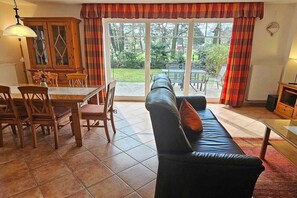 A living room with a sofa, dining table, chairs, and a view through a glass door to an outdoor area. - Holiday home with 3 bedrooms (Ostseebad Prerow)