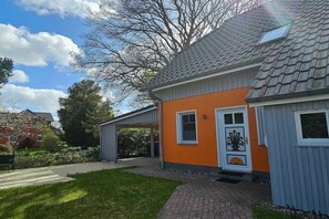 A residential building with a sloped roof, a covered porch, and a front door with a decorative panel. - Holiday home with 3 bedrooms (Ostseebad Prerow)