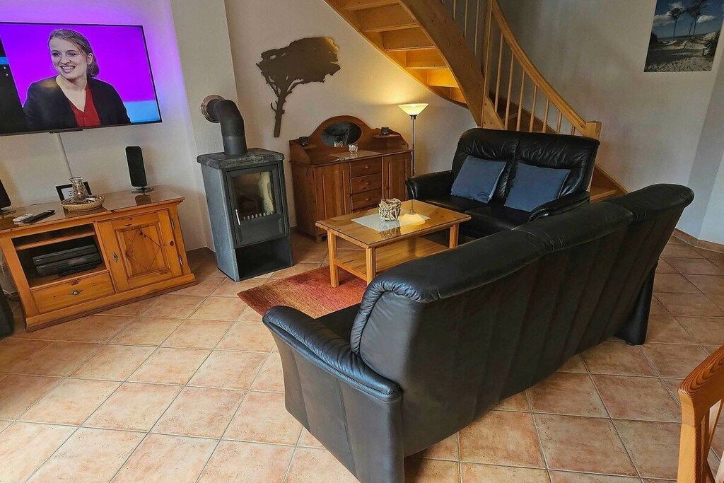 Una sala de estar con un sofá de cuero negro, una mesa de centro de madera, una chimenea y un televisor montado en la pared.