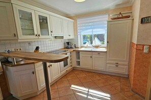 Eine Küche mit weißen Schränken, einer Holzarbeitsplatte, einer Kaffeemaschine und einem Fenster mit Blick auf ein Segelboot.