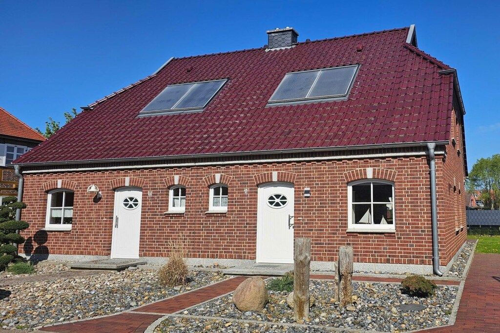 Une maison avec un toit recouvert de tuiles rouges, dotée de deux fenêtres de toit, une façade en briques et une allée gravillonnée.