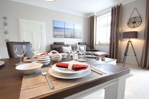 A dining area with a table set for four, a sofa, a lamp, and a wall-mounted compass. - Beach oasis - 1st row by the sea (Ostseebad Binz)