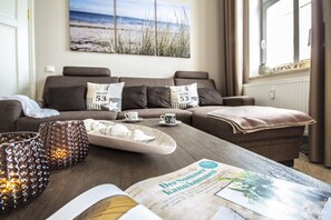 A cozy living room with a brown sofa, a coffee table with a magazine, and decorative candles. - Beach oasis - 1st row by the sea (Ostseebad Binz)