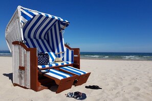 A beach chair with a striped cover, a hat, and a pair of flip-flops on the sand. - Beach oasis - 1st row by the sea (Ostseebad Binz)