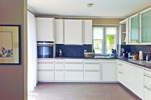 Une cuisine moderne avec des meubles blancs, un four encastré et une fenêtre qui laisse entrer la lumière naturelle.