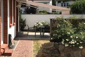 A patio with a table and chairs, a stone wall, and a garden with white flowers. - The Seibert Baltic Sea House (Graal-Müritz)