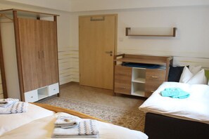 Una habitación de hotel con cama, armario, escritorio y una pequeña estantería.