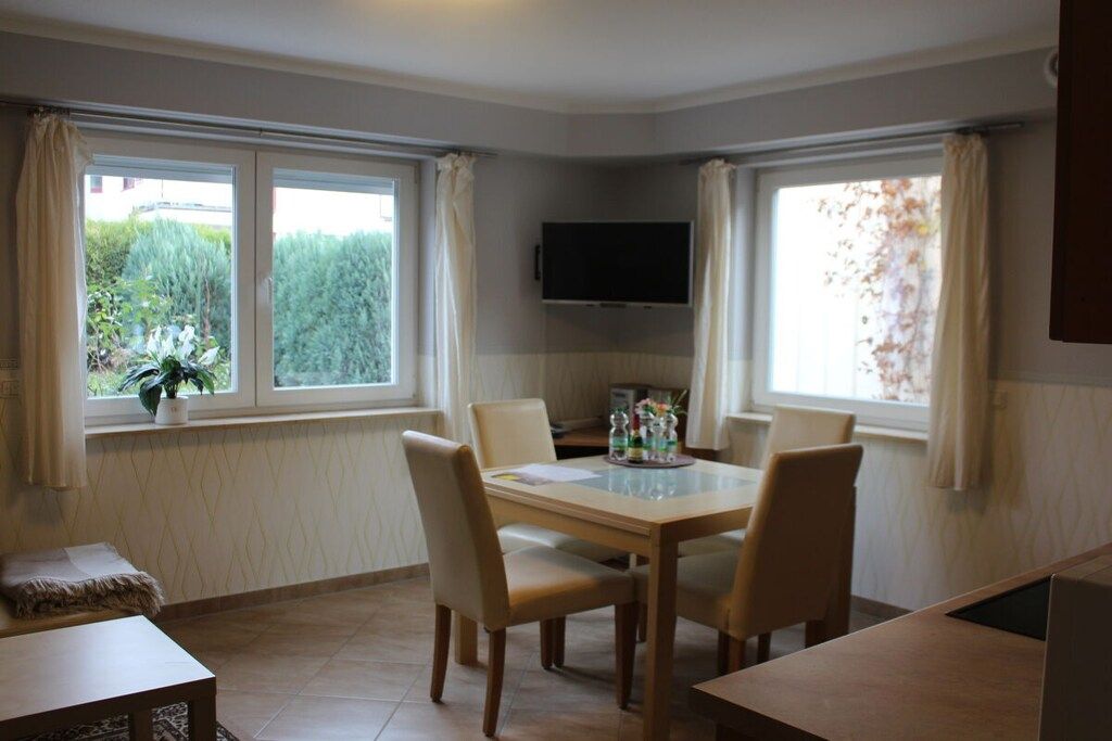 Un comedor con una mesa y sillas, un televisor de pantalla plana montado en la pared y ventanas con cortinas.