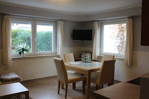 Un comedor con una mesa y sillas, un televisor de pantalla plana montado en la pared y ventanas con cortinas.