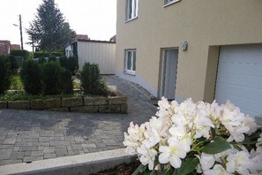 A residential building with a paved driveway, a garage door, and a small garden area with shrubs and flowers. - Holiday apartment with 1 bedroom (Dresden)
