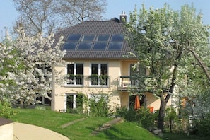 A two-story house with a balcony, surrounded by blooming trees. - Holiday apartment with 1 bedroom (Dresden)