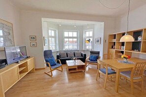 Ein modernes Wohnzimmer mit einer Couch, Sesseln, einem Couchtisch und einem Fernseher auf einer Holzkommode.