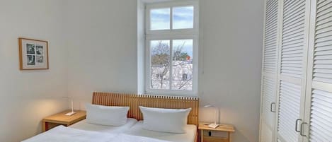 Une chambre à coucher avec un lit, des tables de chevet, une fenêtre et une armoire.