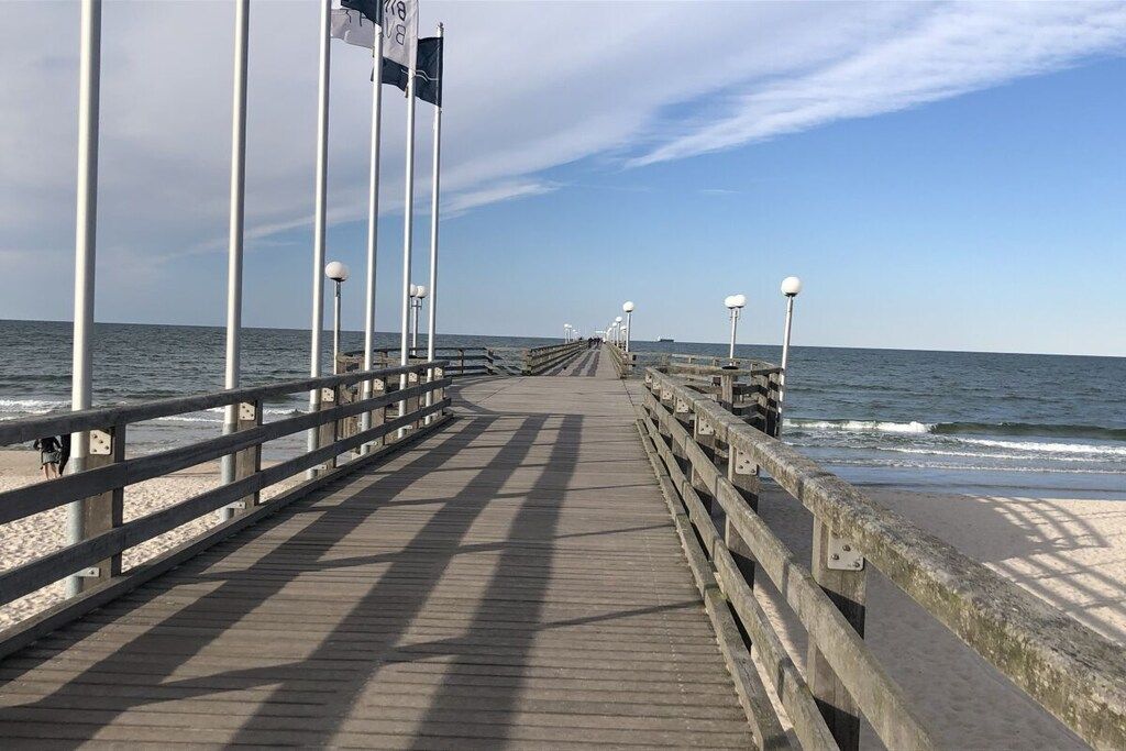 Un paseo marítimo de madera que conduce a la playa, con barandillas y faroles.