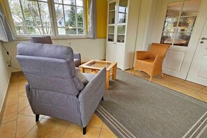 A living room with a grey sofa, a wicker chair, a small wooden table, and a patterned rug. - Holiday home with 1 bedroom (Ostseebad Prerow)