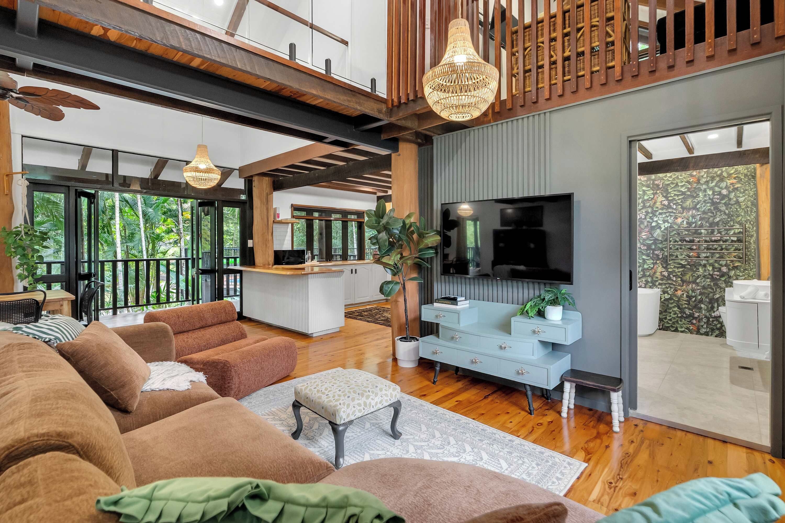 Un vaste espace de vie comprenant un grand canapé, une table basse et un téléviseur fixé au mur. Un balcon avec une rambarde offre une vue sur la verdure environnante.