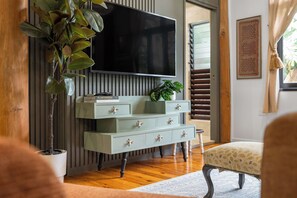 A living room with a television mounted on a wall, a plant, a bookshelf, and a patterned rug. - Treehouse—Serene Tropical Hideaway & Private Pool (Smithfield)