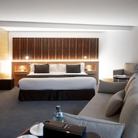 Una habitación de hotel moderna con una cama grande, un sofá, una mesita y un panel de luz empotrado en la pared.