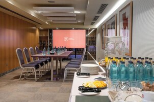 Un salón de conferencias con una larga mesa, sillas, una pantalla de proyector y una mesa de buffet con comida y bebidas.